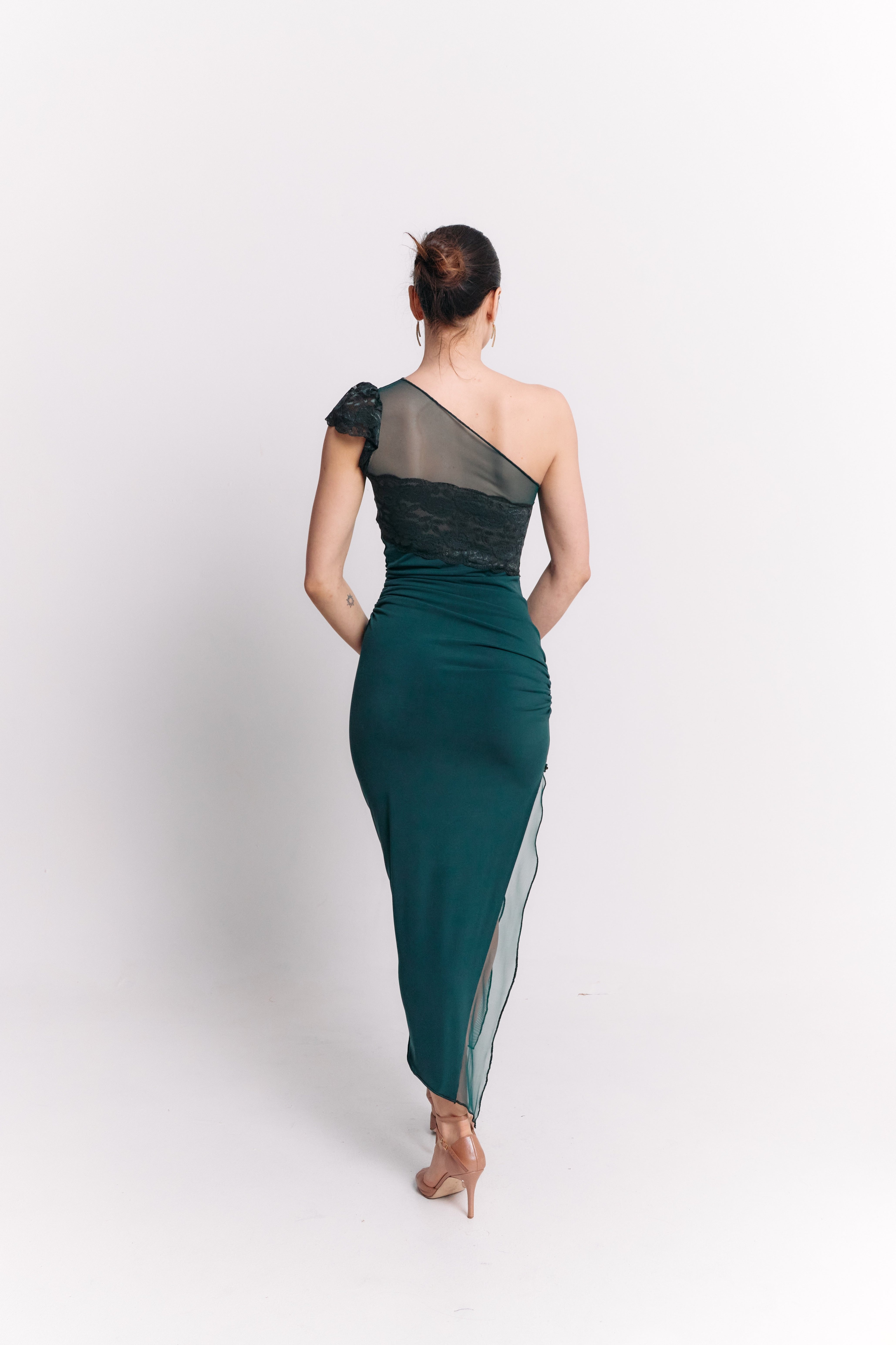 Woman wearing a one-shoulder green dress with black mesh overlay on a white background