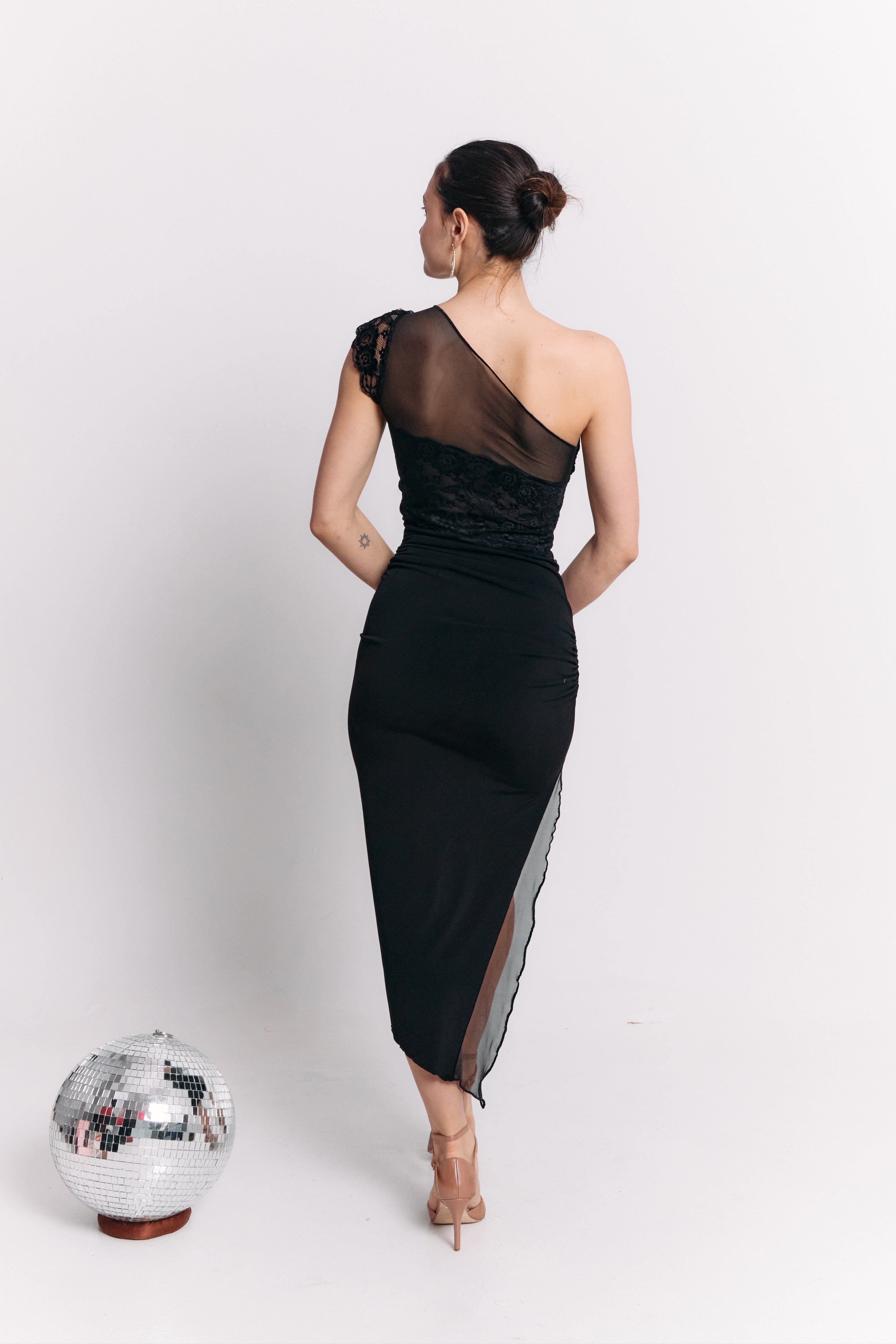 Woman wearing a black one-shoulder dress with a silver disco ball on a white background